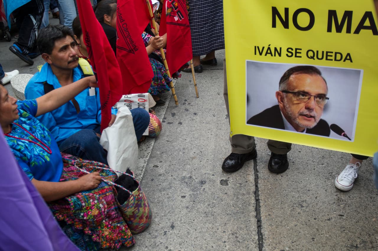 Gente sentada junto a un cartel con una fotografía de Iván Velasquez, comisionado de la Comisión Internacional Contra la Impunidad de Guatemala creada por Naciones Unidas, con el mensaje "Iván se queda", el sábado 26 de agosto de 2017 en Ciudad de Guatemala. (AP Foto/Moisés Castillo)