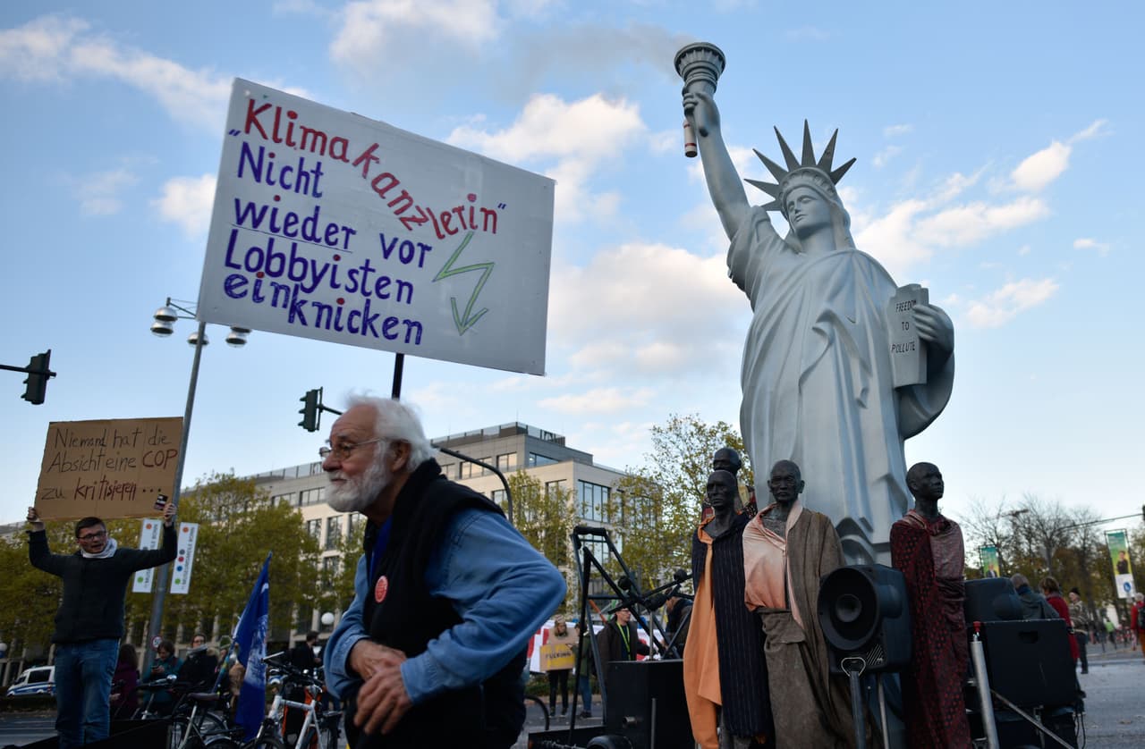 Una maqueta de la Estatua de la Libertad emitiendo humo y un cartel que pide a los negociadores que no cedan en la lucha contra el cambio climático son parte del paisaje actual en Bonn.