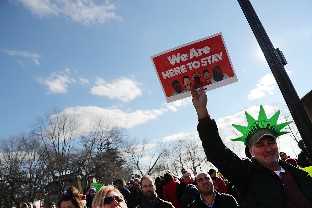 Un manifestante con un gorro de la Estatua de la Libertad y un cartel que dice "Estamos aquí para quedarnos" durante la protesta en Nueva York.