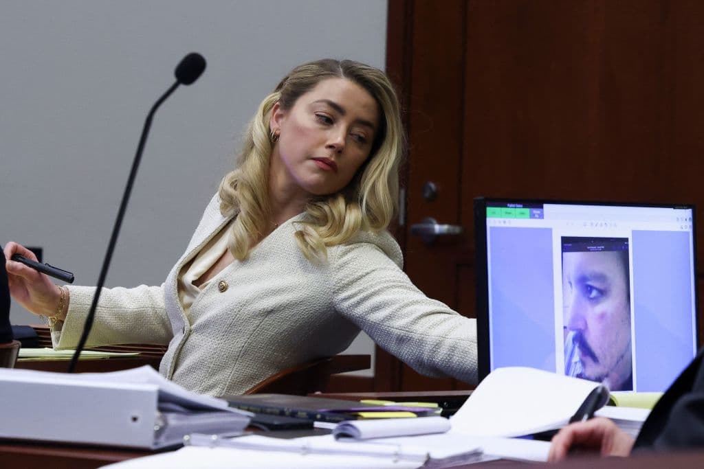Amber Heard escucha a su exmarido Johnny Depp, mientras se ve en la pantalla una imagen de una herida en el rostro del actor, durante el juicio por difamación contra ella.