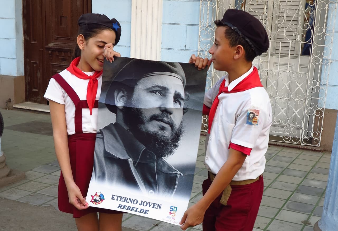 Dos pioneritos sostienen un retrado de Fidel joven en una calle de Cienfuegos, Cuba, el 30 de noviembre.
