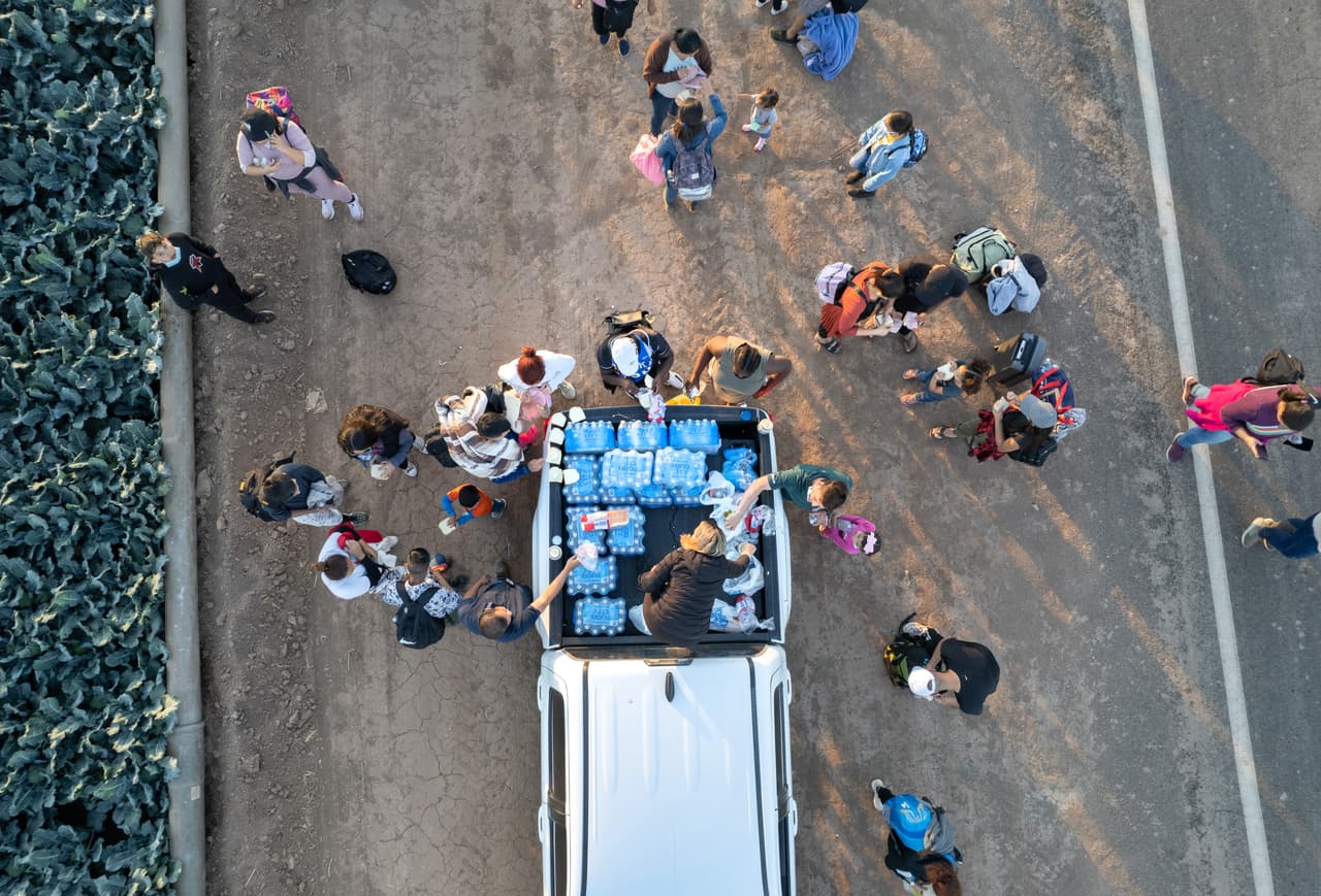 Desde esta panorámica aérea se observa a los inmigrantes cuando se detienen para agarrar agua gratis de los buenos samaritanos mientras caminan desde la frontera entre Estados Unidos y México hasta un centro de detención de la Patrulla Fronteriza en la ciudad de Yuma, Arizona. Los agentes de la Patrulla Fronteriza habían dicho anteriormente que las instalaciones estaban llenas y luego habían dejado de transportar migrantes desde la frontera hasta el centro. Entonces, algunos migrantes caminaron los siete millas hasta allí por su cuenta.