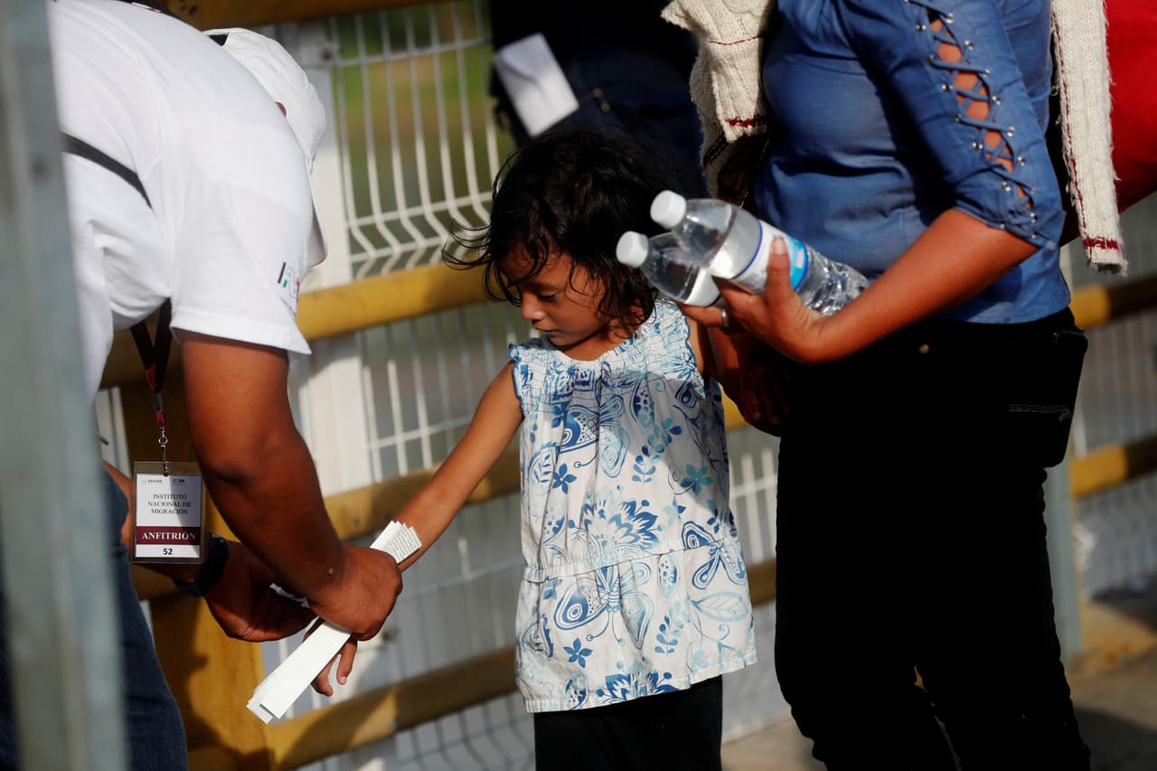 Autoridades mexicanas colocan un brazalete a una niña migrante hondureña para que pueda ingresar al territorio mexicano.