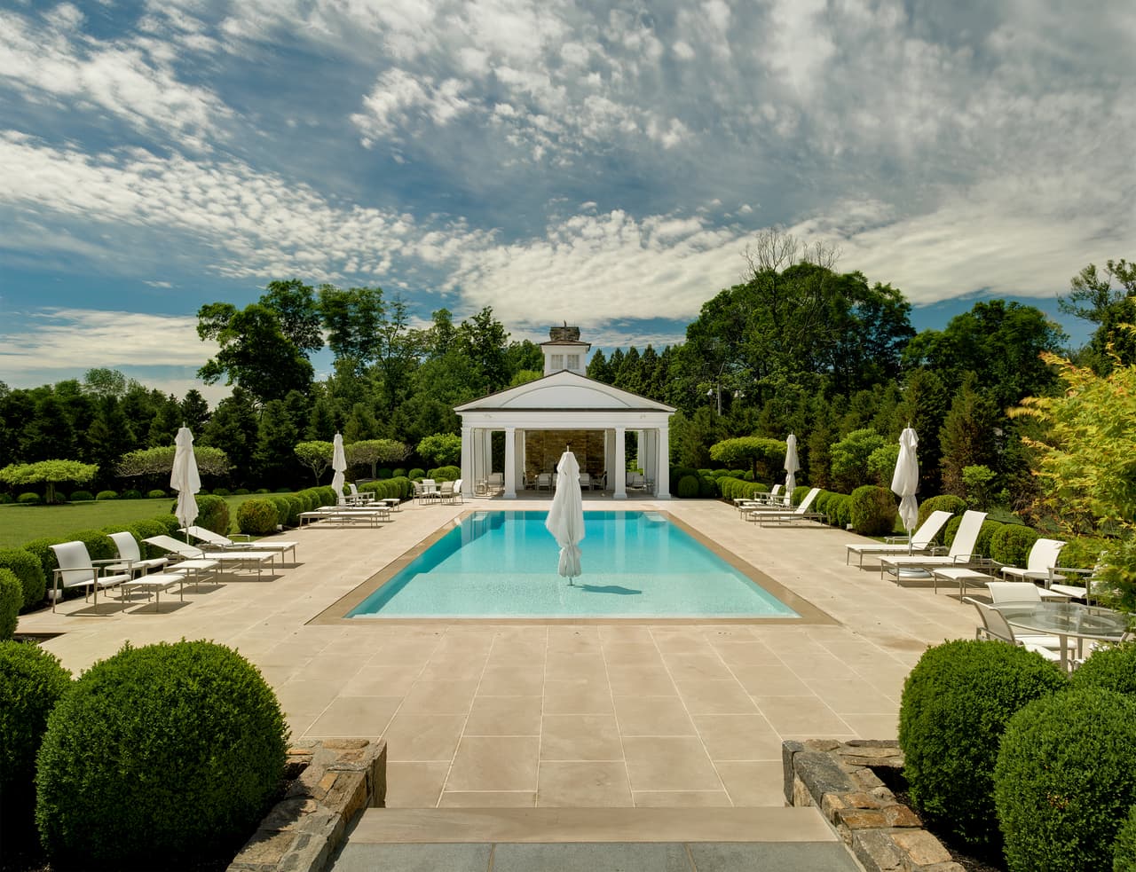 Una amplia piscina rodeada de árboles se ubica en la parte posterior de la elegante mansión.
