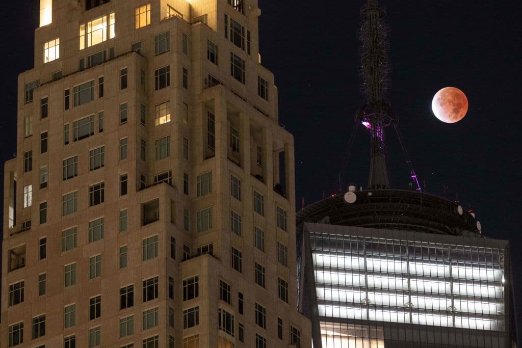 En la imagen, una luna llena casi completamente cubierta por la sombra es vista desde el One World Trade Center de Nueva York la madrugada de este viernes.
