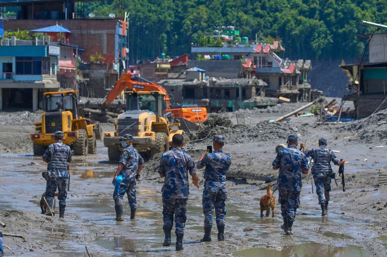 Policías nepalíes observan cómo las excavadoras retiran los escombros de las inundaciones repentinas en el distrito de Nuwakot, Nepal.