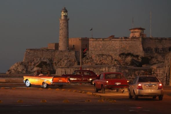 Aquí vemos un grupo de coches viejos y nuevos circular en el barrio de La Habana Vieja, con el Castillo de San Felipe del Morro como fondo.