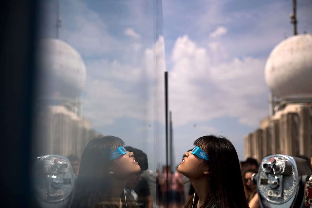 <b>Los lentes:</b> fueron la forma más común de apreciar el eclipse. En la imagen, una joven ve el fenómeno desde el imponente Rockefeller Center, en Nueva York. Drew Angerer/ GettyImages