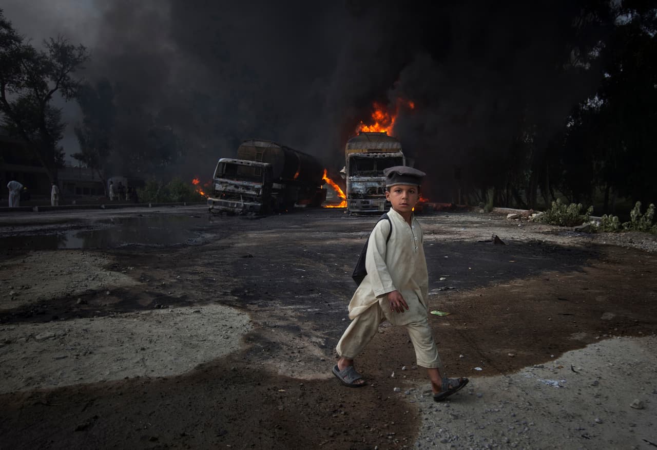 <b>Pakistán.</b> Un niño de camino a la escuela frente unos camiones incendiados en una carretera de Pakistán, donde pistoleros interceptaron varios vehículos de suministro de la OTAN. 7 de octubre de 2010.
