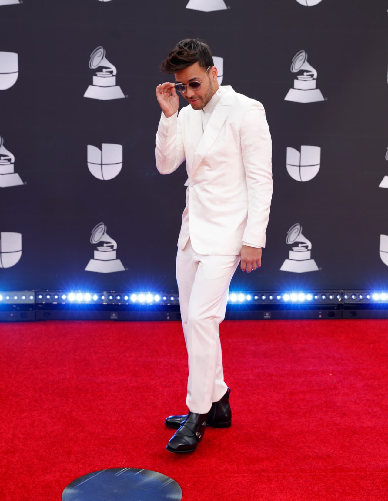 El cantante Prince Royce, con un traje color blanco y gafas oscuras a su paso por la alfombra roja de La 20a. Entrega Anual de Latin GRAMMY.