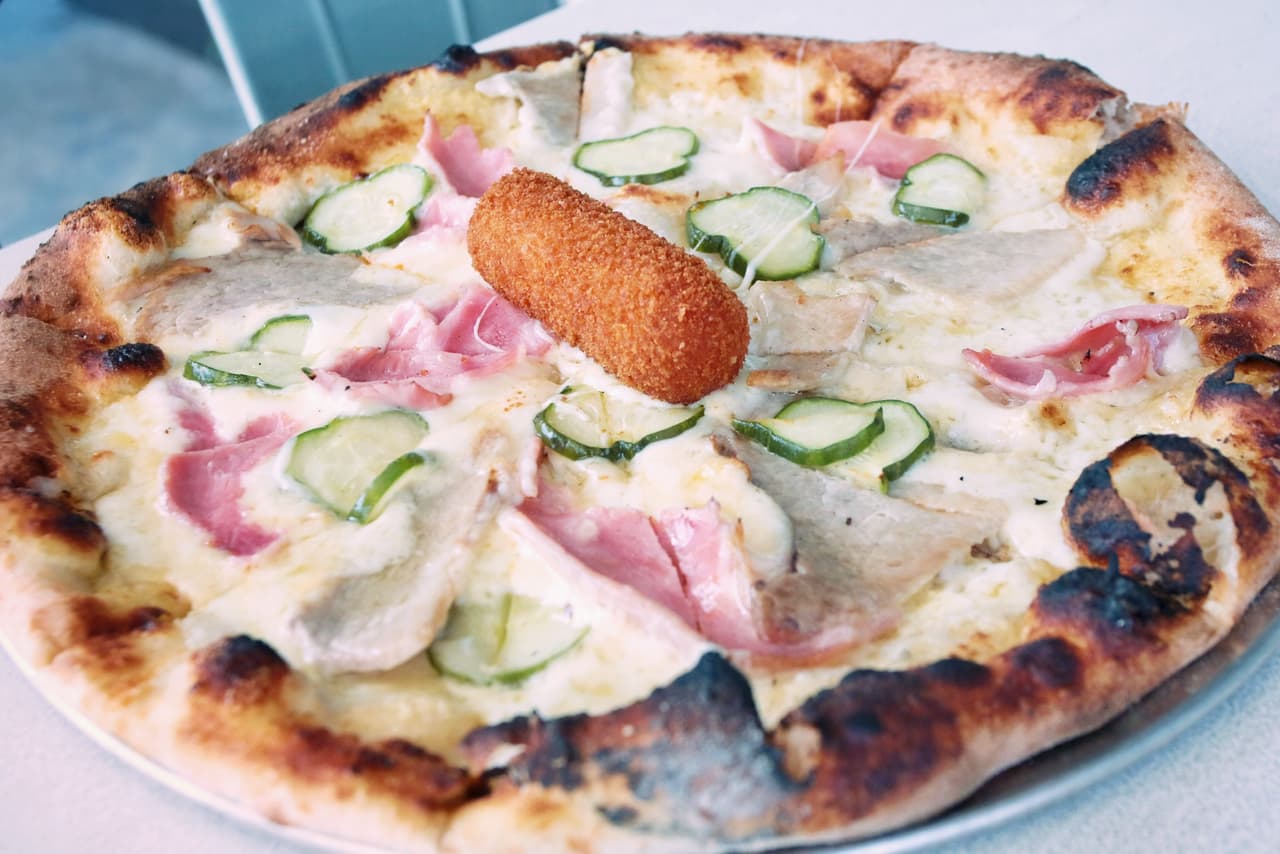 Esta pizza lleva el puerco asado y el jamón glaseado que preparan en el Versailles, pepinillos empanizados con mantequilla, queso fontina y gruyère y salsa de mostaza. El toque mágico es una de sus famosas croquetas cubanas en el centro de la pizza.