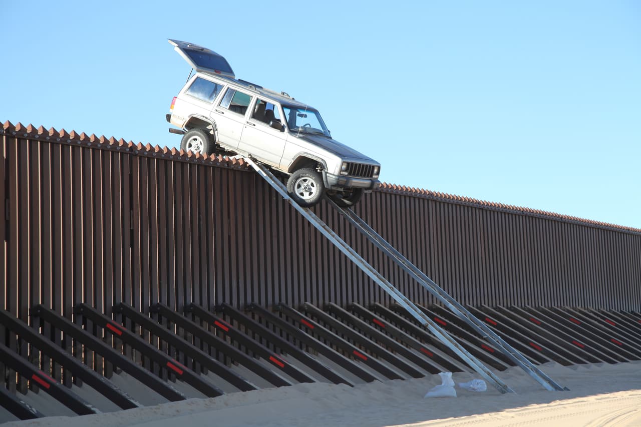 <b>1. Una camioneta Cherokee atascada en el punto más alto del muro.</b> Esta foto es real. Fue tomada por la agencia AP el 31 de octubre de 2012 y registra la descabellada idea de unos contrabandistas de hacer pasar un jeep Cherokee por el muro que divide la frontera entre EEUU y México, que mide los poco desestimables 14 pies. Con unas rampas artesanales que dispusieron de lado y lado, los creativos criminales intentaron subir el carro hasta el punto más alto y, de hecho, lo lograron. No contaron, sin embargo, con que el carro corría el riesgo de atorarse. 
<br>