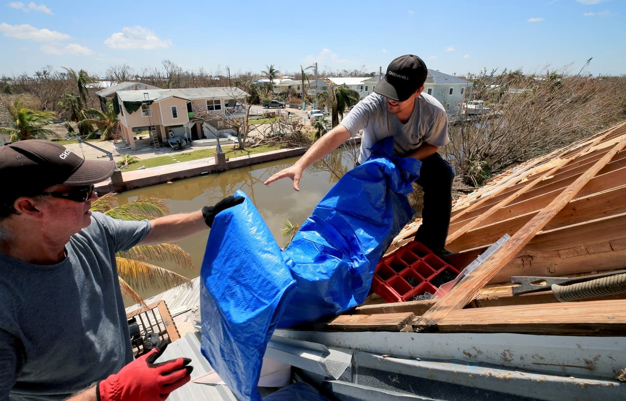 Bob Fiorile, de 72 años, y Todd Brown, de 42 años, a la derecha, tiran una lona al techo expuesto de la casa de Fiorile en Big Pine Key. Los residentes fueron autorizados a regresar a sus casas una semana después de que el huracán Irma golpeara los Cayos de la Florida.