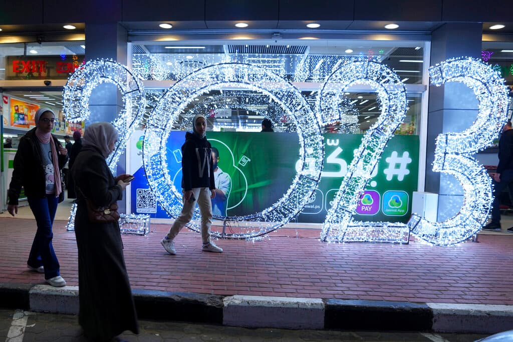 Niñas palestinas se toman fotos frente a números iluminados por el nuevo año 2023, en la carretera principal de la ciudad de Gaza, en la noche de Año Nuevo.