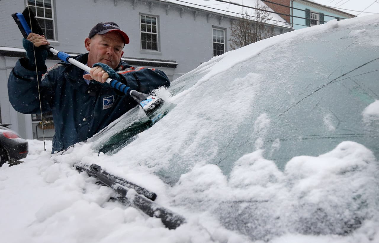 Buddy Collins, un empleado de correos raspa el hielo y la nieve del parabrisas de su auto