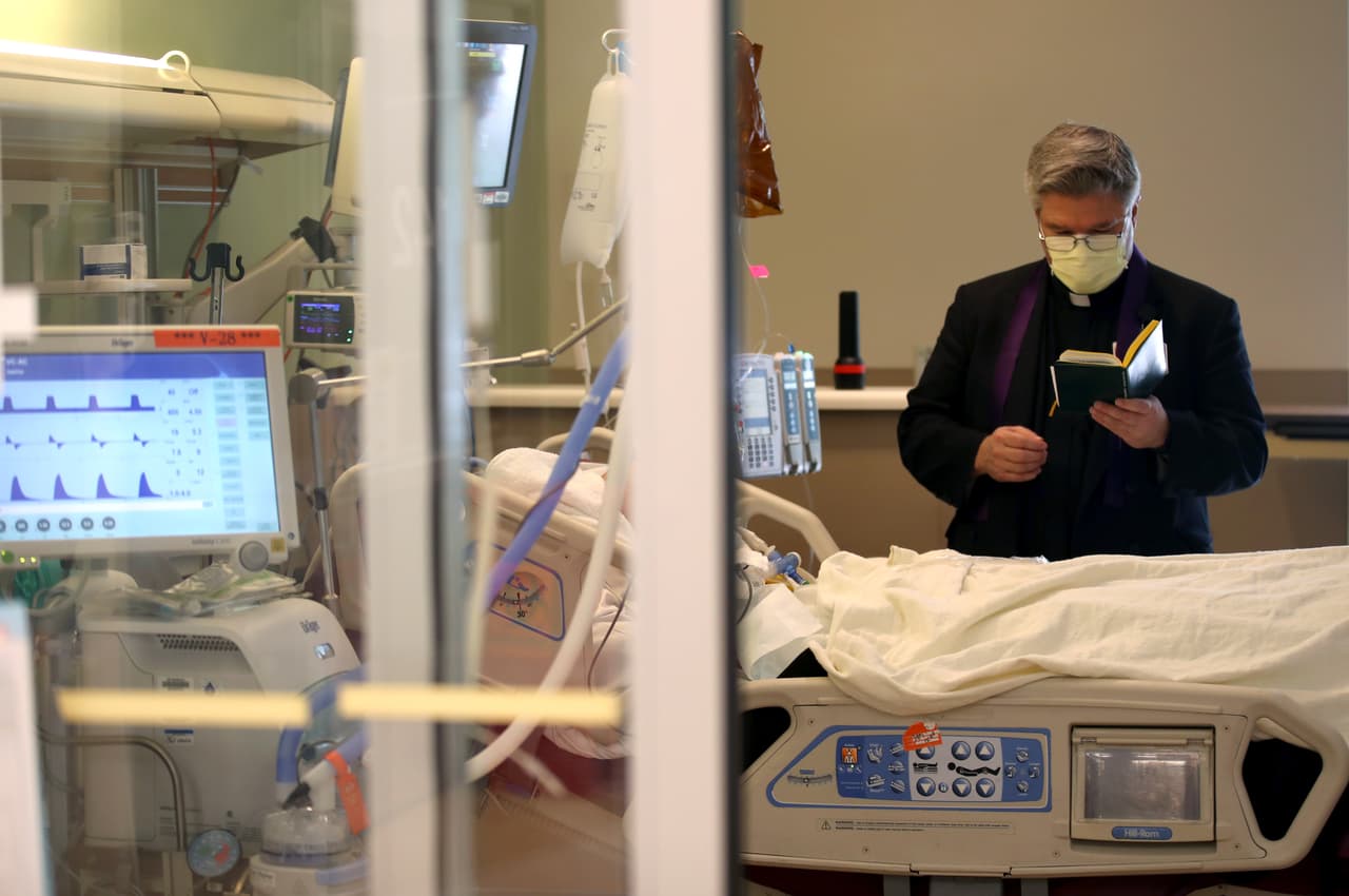 El padre Barry O'Toole ora con un paciente internado en una unidad de cuidados intensivos en un hospital de San José, en California, el 21 de mayo de 2020.