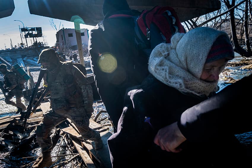 Soldados del ejército ucraniano reaccionan al sonido de los disparos del ejército ruso mientras una anciana en silla de ruedas está siendo evacuada de la ciudad de Irpin.