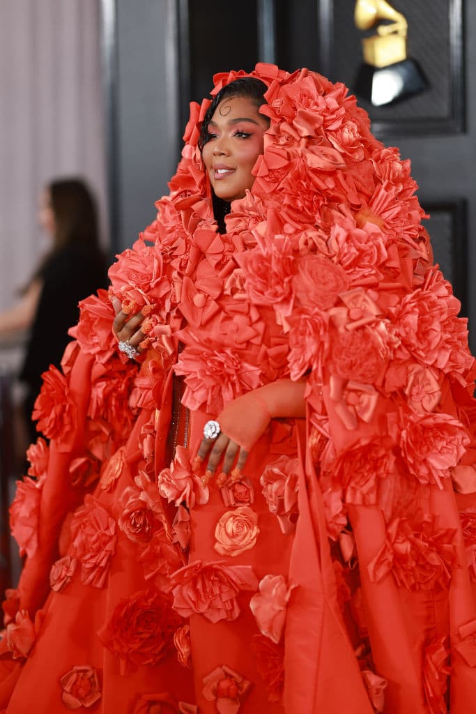 <h2 class="cms-H2-H2">Lizzo</h2>
<br>La cantante, rapera y compositora desfiló por la alfombra roja con un original outfit en color naranja, que incluía una capa del mismo color y con flores en releve.