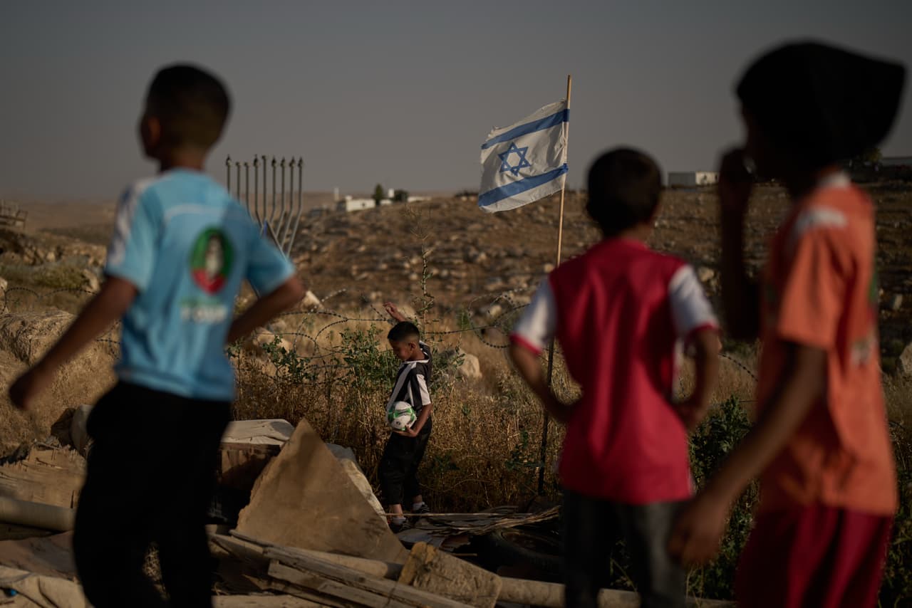 Un niño palestino recupera un balón de fútbol que cayó más allá de una valla de alambre de púas erigida por colonos israelíes junto a un campo de fútbol en la aldea beduina de Umm al-Khair, en Cisjordania, el martes 12 de mayo de 2026. (Foto AP/Leo Correa)
