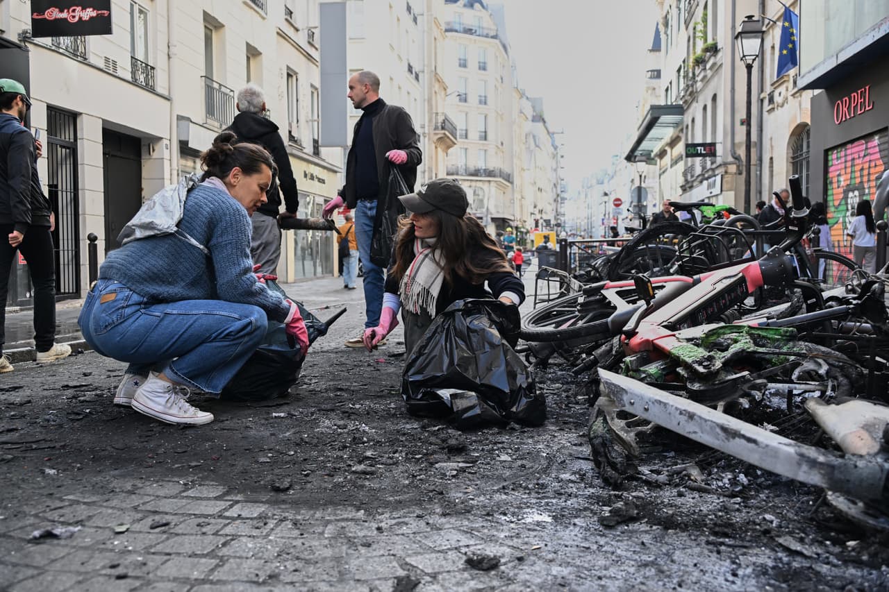 Varias personas limpian los escombros en una calle junto a bicicletas quemadas al día siguiente de una manifestación contra el aumento del costo de vida y en solidaridad con las reivindicaciones estudiantiles, en París, el domingo 18 de octubre de 2026.