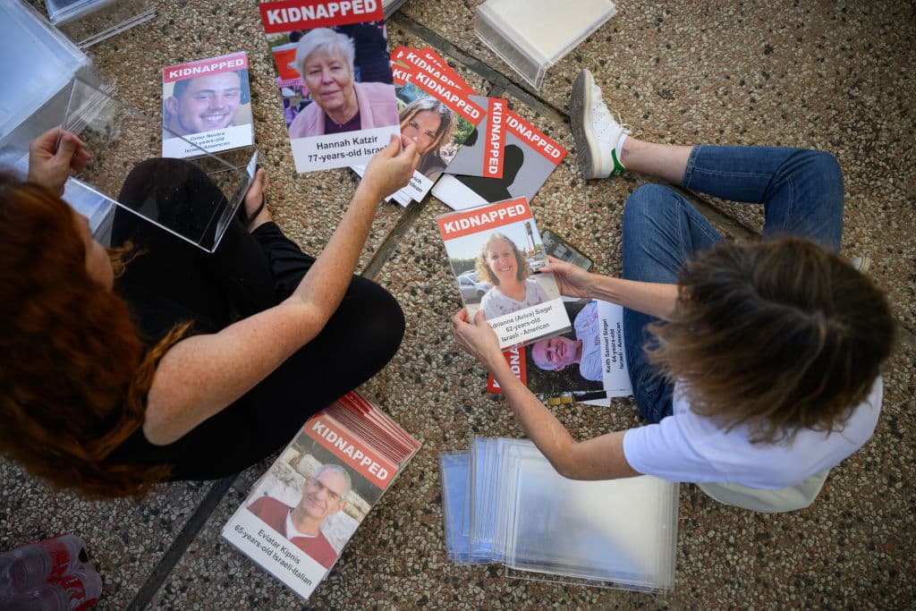 Dos personas ven fotografías de los desaparecidos este viernes mientras se prepara una mesa de 'Cena de Shabat' en la plaza del museo de Tel Aviv, con 200 asientos vacíos, que representa a los rehenes y personas desaparecidas.