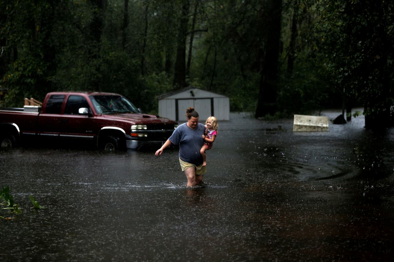 Una mujer con un niño en brazos trata de alejarse de una zona inundada en el condado de Duplin, Carolina del Norte. Las autoridades temen que se produzcan deslizamientos de tierra en las laderas de los Apalaches en las Carolinas. 
<br>
