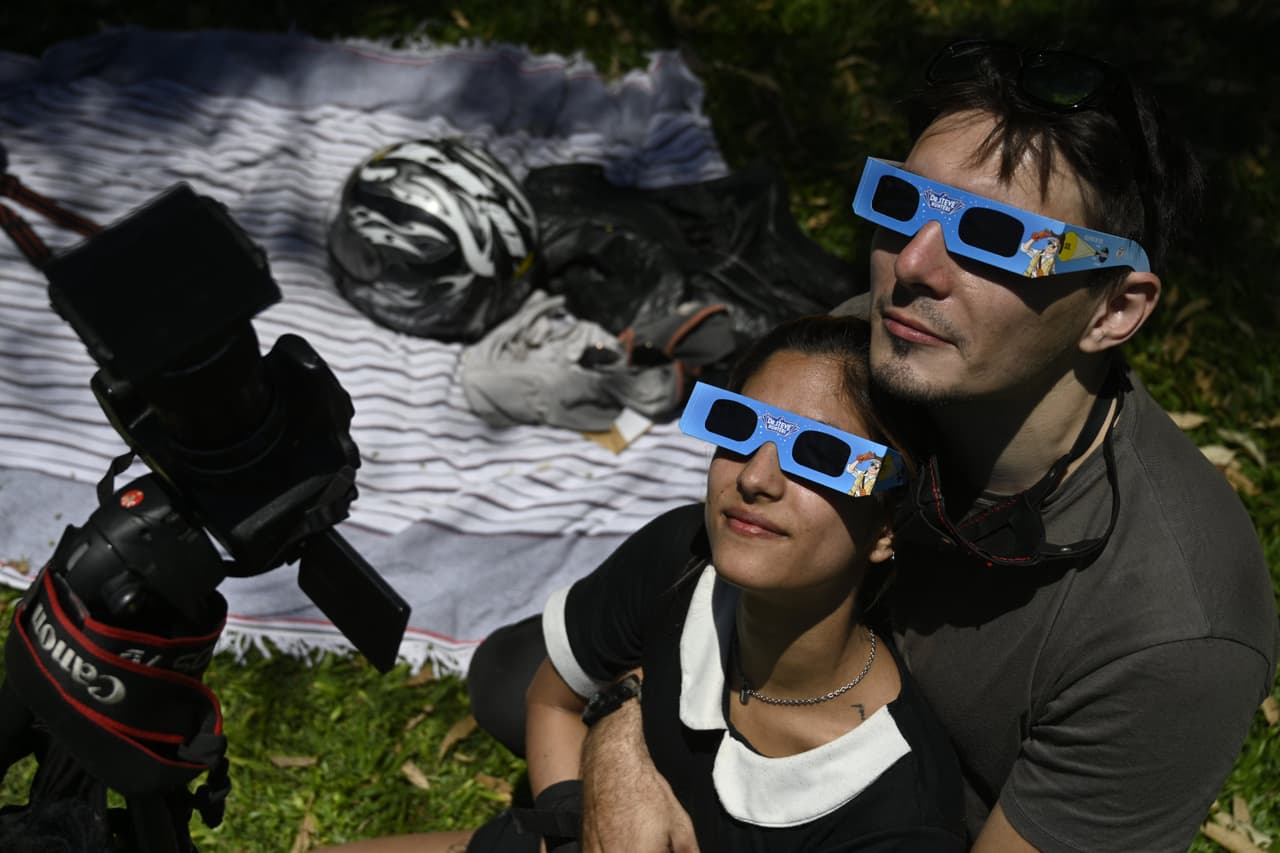 Una pareja observa y toma fotografías del eclipse solar en el parque del planetario Galileo Galilei en Buenos Aires.
<br>
<br>El fenómeno pudo verse en todo el país con distintos grados de precisión. En la ciudad de Buenos Aires, ubicada al norte de la "franja de totalidad", se pudo ver una cobertura máxima del 79% y uno de los puntos de mayor afluencia para observarlo fue el planetario.