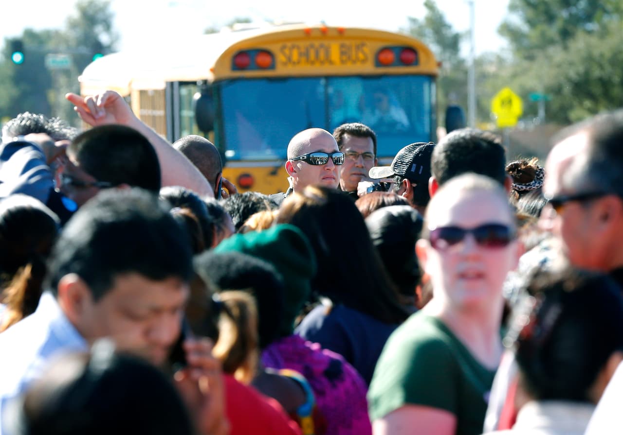 A Phoenix police officer, center, tries to give instructions to parents waiting to board buses to reunite with their children, Friday, Feb. 12, 2016, in Glendale, Ariz., after two students died in a shooting at Independence High School in the Phoenix suburb. The danger at the campus was over, police said, as worried parents crowded stores nearby to await word on their children.(AP Photo/Matt York)