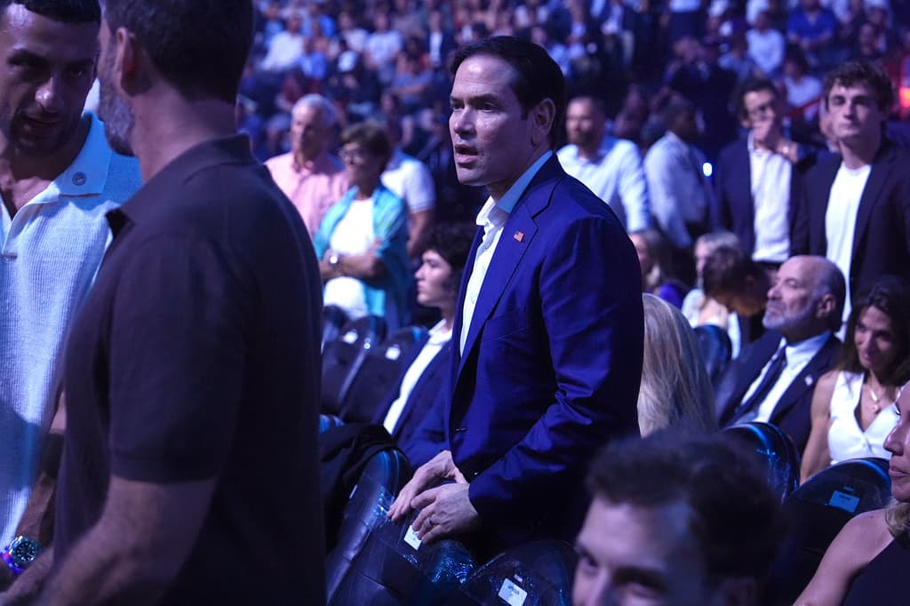 Al igual que otros asistentes, 
<b><a href="https://www.univision.com/noticias/estados-unidos/negociaciones-eeuu-iran-marco-rubio-ya-negocia-aspectos-del-programa-nuclear-irani" target="_blank">el secretario de Estado, Marco Rubio,</a> </b>prefirió ponerse en pie para poder 
<b>observar mejor la acción</b> que se desarrollaba en el octágono.