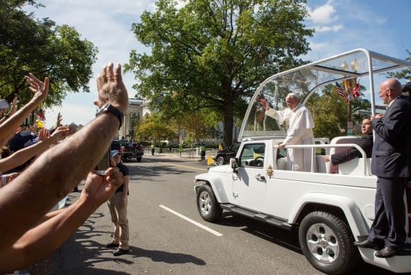 Las manos saludando al pontífice que viaja en el Papamóvil.