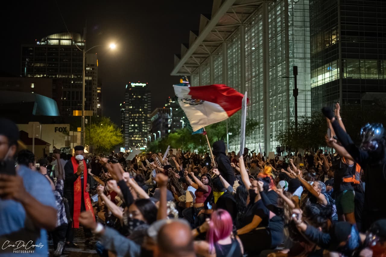 En medio de la protesta se observa a manifestantes portando la bandera de México mientras recorren las calles de Phoenix, Arizona.