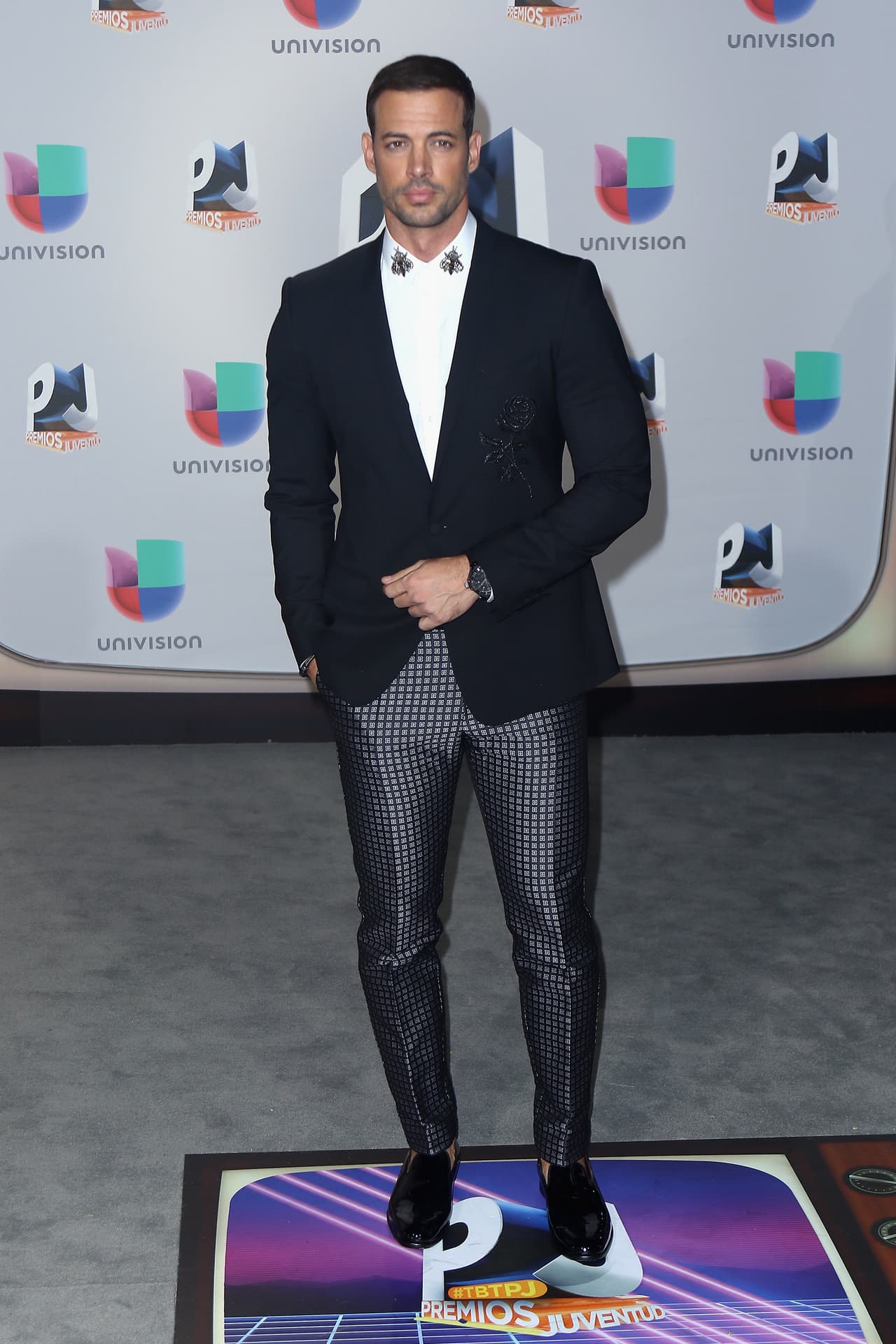 William Levy dio lecciones de estilo en la alfombra de los premios Juventud. Con un saco de abotonadura sencilla perfecto para su cuerpo, unos pantalones brillantes y un floral bordado en su camisa, este famoso hizo ver que los hombres si tienes otras posibilidades para la formalidad.