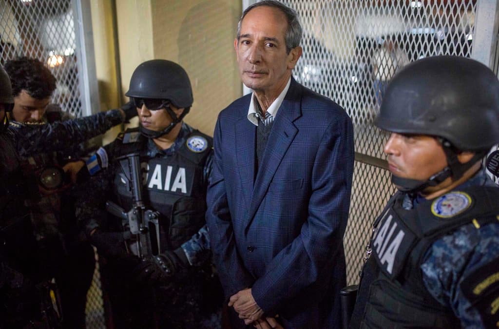 Former Guatemalan President Alvaro Colom is flanked by police in a courtroom in Guatemala City, Tuesday, Feb. 13, 2018. Colom, who governed from 2008 to 2012, has been detained in a corruption case according to special prosecutor Juan Francisco Sandoval.