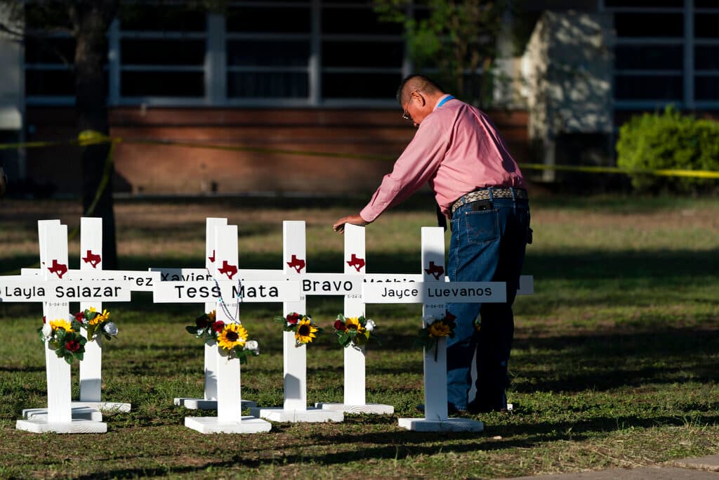 El pastor Daniel Myers coloca su mano sobre cruces con los nombres de las víctimas del tiroteo del martes en la Escuela Primaria Robb en Uvalde,