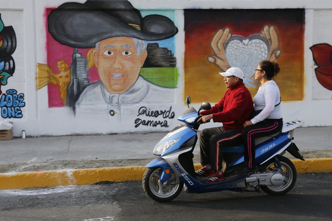 Una pareja sobre una motocicleta mira un mural en donde Francisco porta un sombrero de charro.