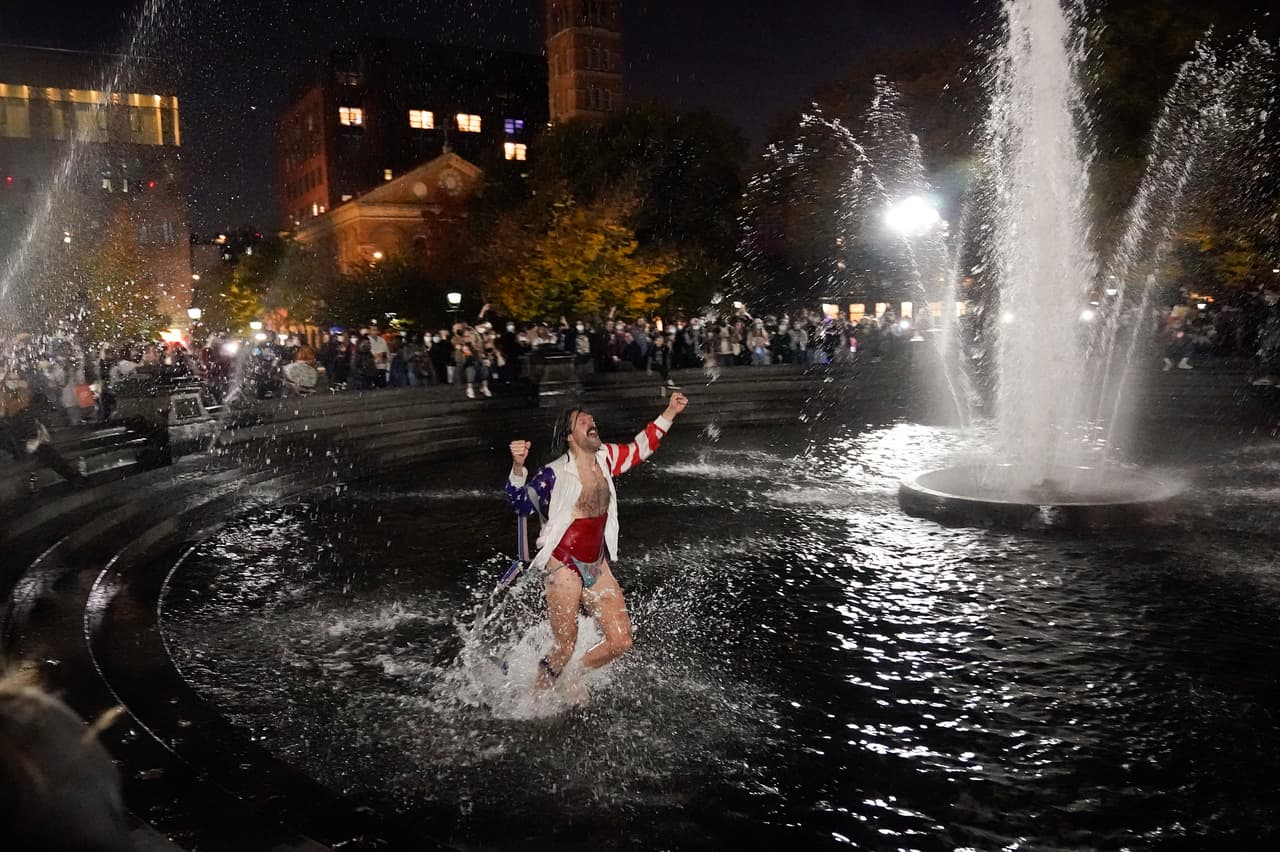 Un hombre baila en la fuente mientras asiste a una reunión en Washington Square Park para celebrar el triunfo de Joe Biden.