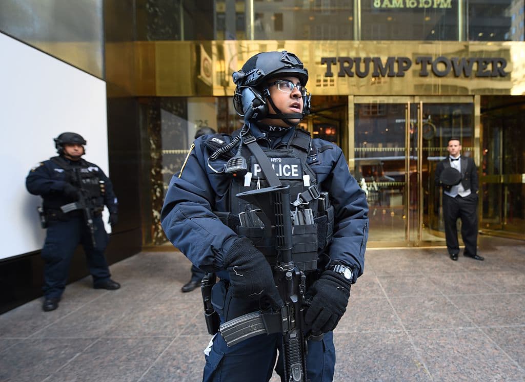 La imagen de la entrada a la Torre Trump incluye policías con armas largas al lado de un portero vestido impecablemente con lazo y chaleco.