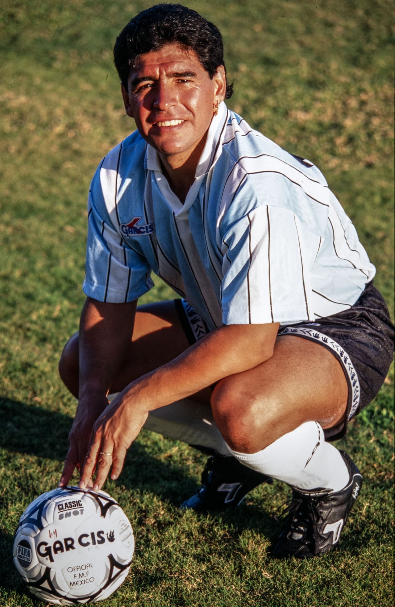 En la tradicional posee de futbolista e los años 90 y anteriores, con las manos en la pelota.