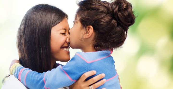 family, children and happy people concept - happy little girl hugging and kissing her mother over green background