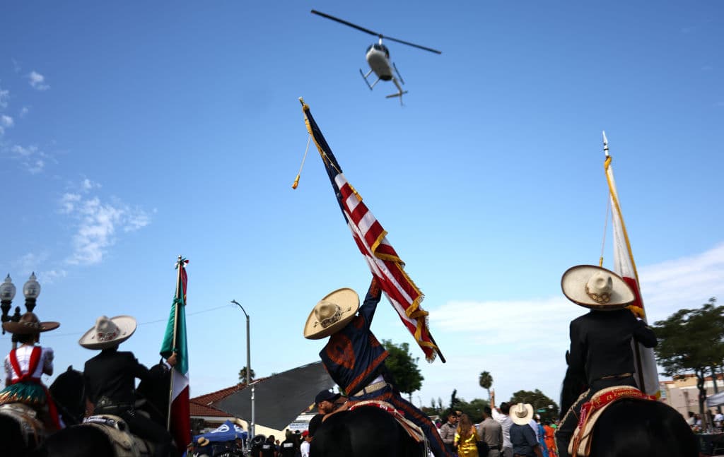 A la presencia de un inesperado helicóptero, participantes en el Desfile por la Independencia de México en Los Ángeles reaccionaron mostrando la bandera de Estados Unidos.