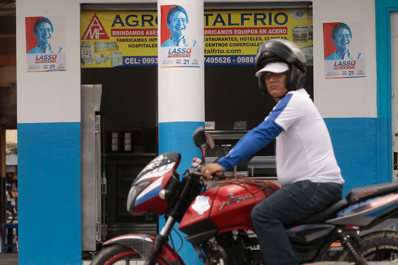 Un hombre pasa delante de un comercio con propaganda de Lasso.