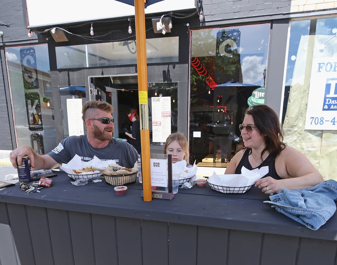 Martin Benisek, Emily y Katie Benisek almuerzan el viernes en la acera frente al restaurante Scratch Kitchen and Lounge en Forest Park. Los clientes de restaurantes deben comer afuera de los locales según las normas establecidas en la tercera fase del plan de reapertura.
