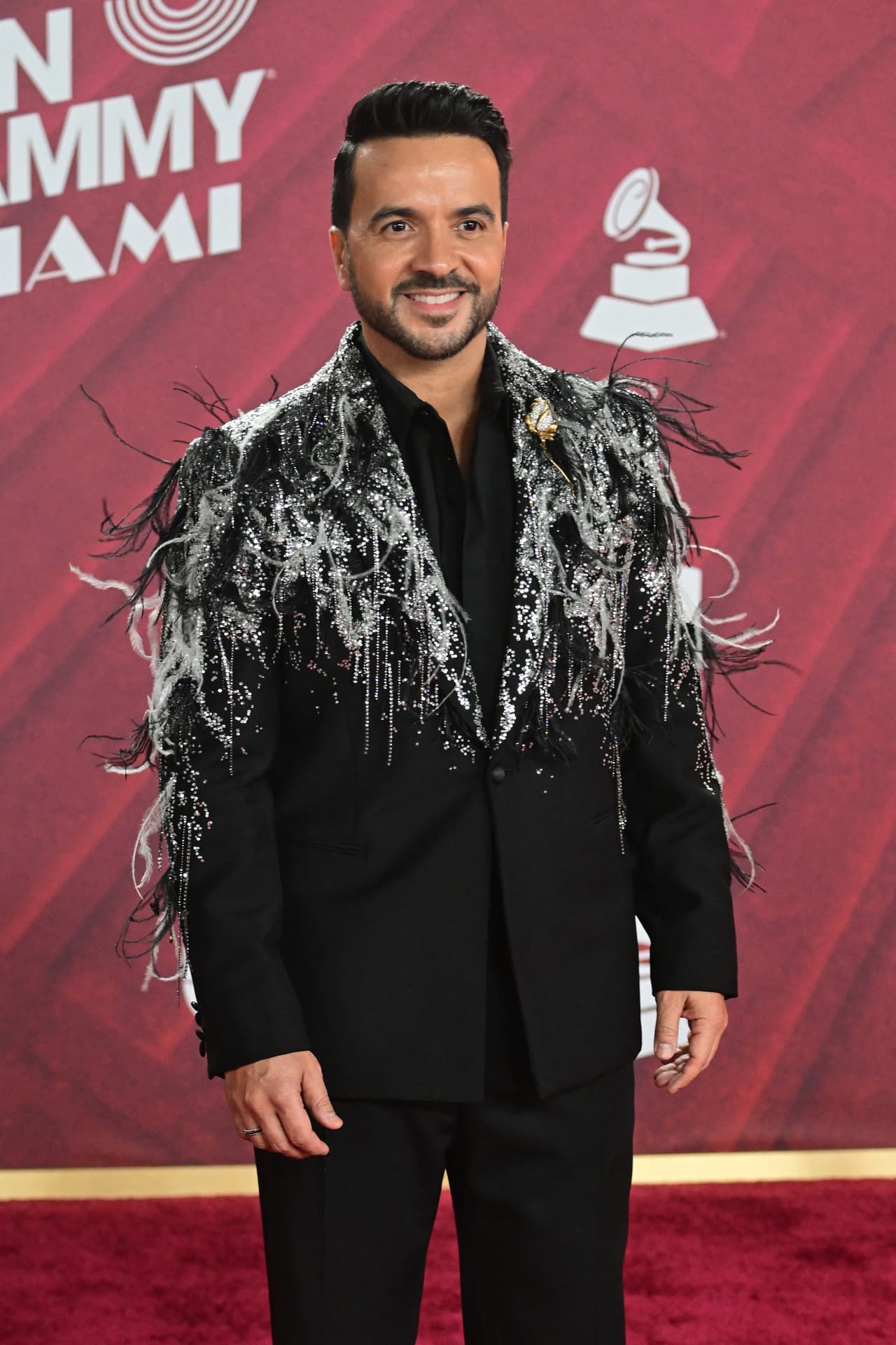 <b>Luis Fonsi </b>contrastó su look negro con los brillos y plumas de su saco.
