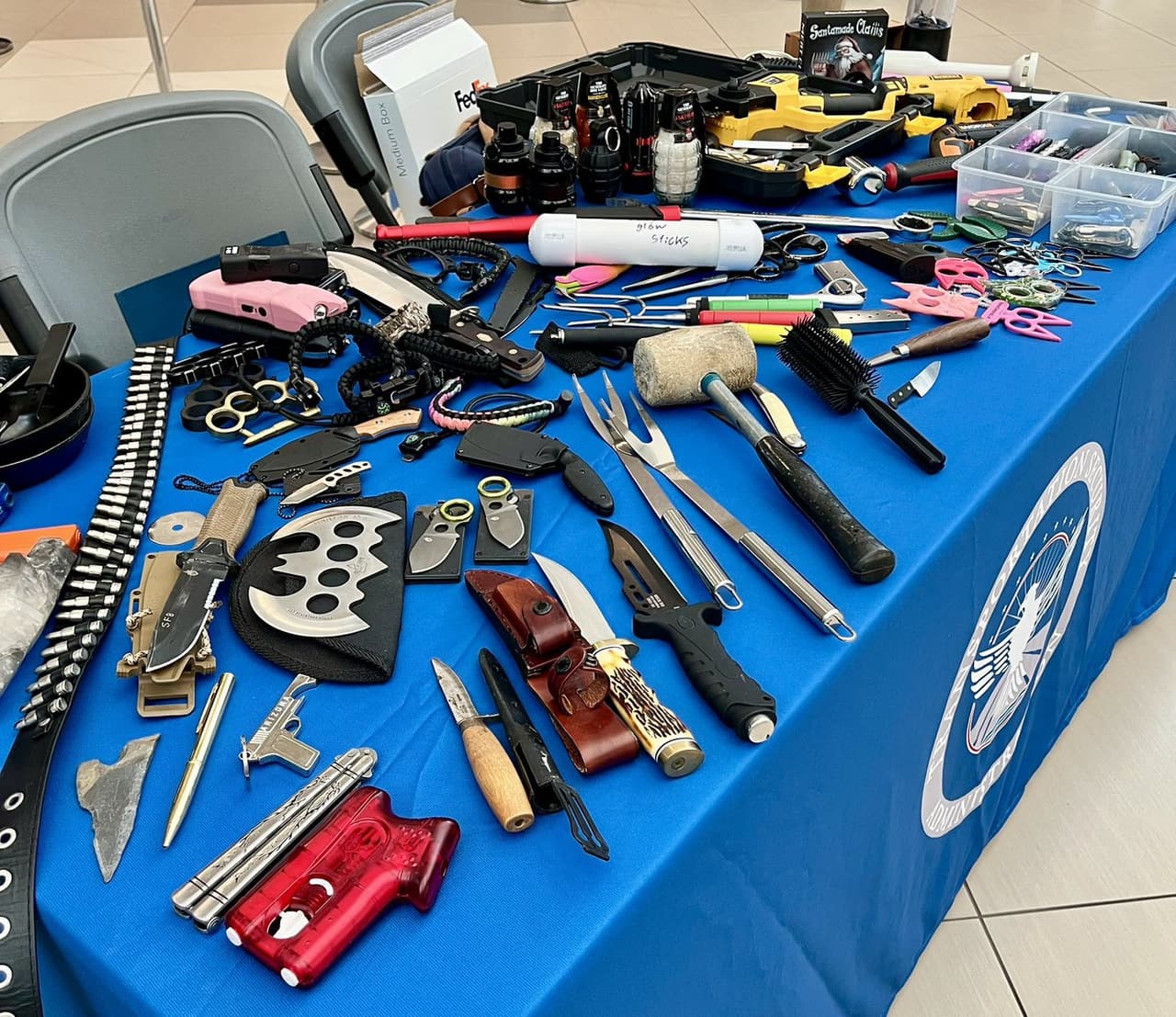 Una mesa de la TSA llena de artículos prohibidos confiscados, que incluyen una gran variedad de cuchillos, armas de electrochoque (táseres), manoplas de metal y supuestas granadas de mano.