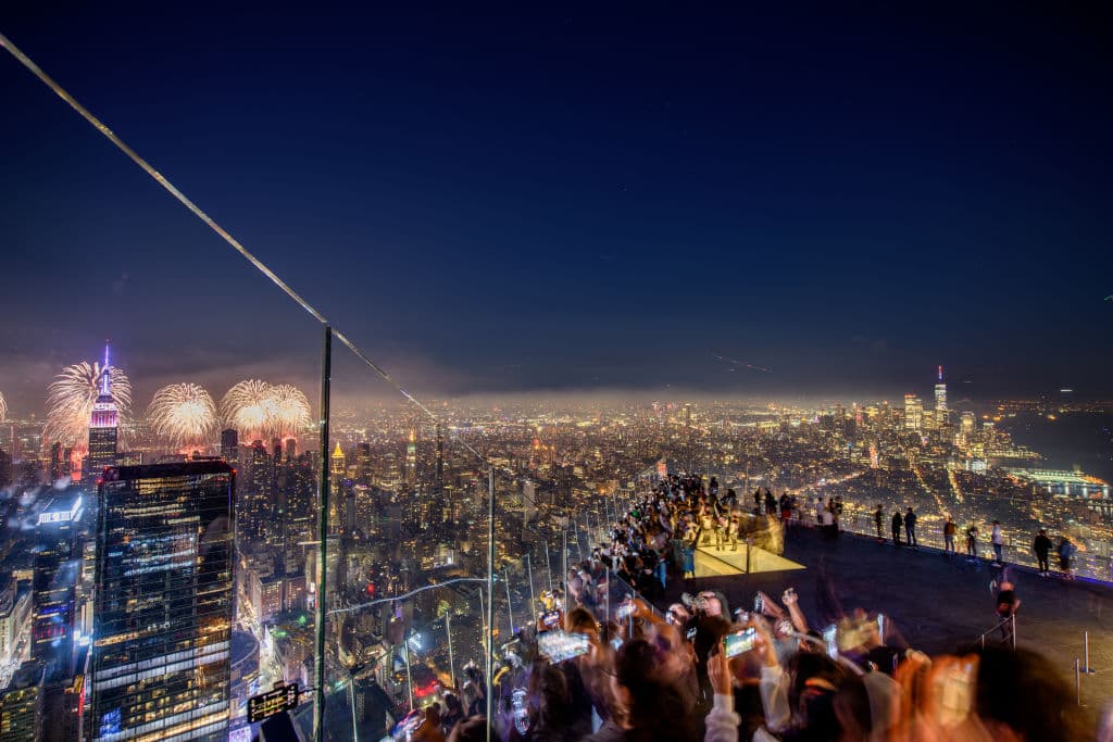 Personas contemplan los espectaculares fuegos artificiales de Nueva York desde el Hudson Yard. La ciudad ha visto a sus íconos, como la 'Torre de la Libertad', la estación de Grand Central, varios de los puentes sobre el río Hudson y otros conocidos edificios, teñidos de colores de la bandera estadounidense este 4 de julio.
