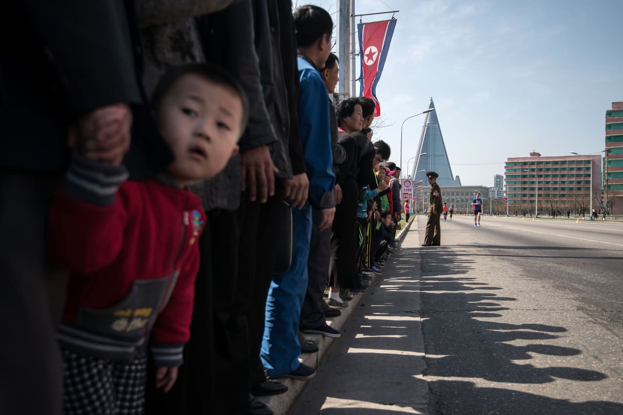 Un niño en la ruta del maratón de Pyongyang. Al fondo se ve la silueta piramidal del hotel Ryugyong. La estructura de 105 pisos empezó a levantarse en 1987 pero se detuvo en 1992 cuando Corea del Norte empezó a travesar una dura crisis económica tras la caída de la Unión Soviética.