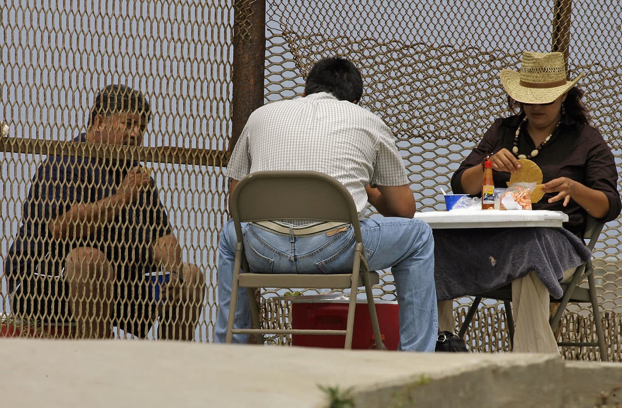 Una familia mexicana comparte el almuerzo a través de la cerca fronteriza en Tijuana en 2007. El encuentro de migrantes con sus documentos en regla y sus familiares del lado mexicano a través de esta valla se hizo común a través del tiempo. La cerca divisoria entre Estados Unidos y México en la zona de Tijuana-San Diego tenía ya casi 20 años para el momento en que se tomó esta fotografía.