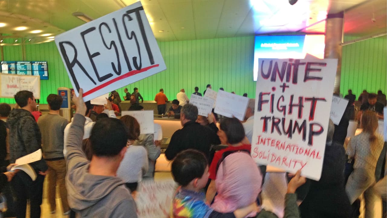 Una mujer de padre paquistaní con su hijo en brazos levanta un cartel contra Trump.