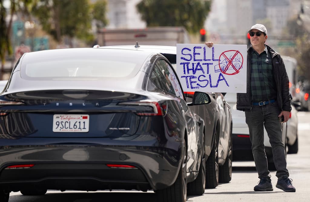 Un manifestante sostiene un cartel que dice "SELL THAT TESLA" (Vende ese Tesla) frente a un conductor de Tesla durante una protesta afuera de un concesionario de Tesla en San Francisco, el sábado 15 de marzo de 2025. (AP Foto/Josh Edelson)