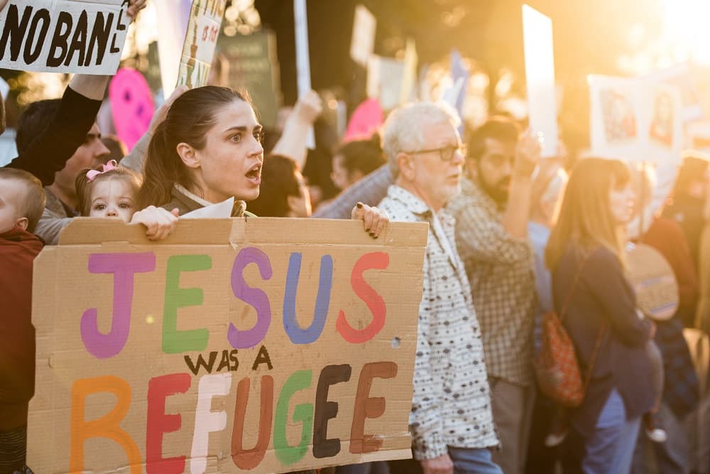 Una joven con un cartel donde se lee "Jesús era un refugiado" durante una protesta contra la orden ejecutiva migratoria de Donald Trump.